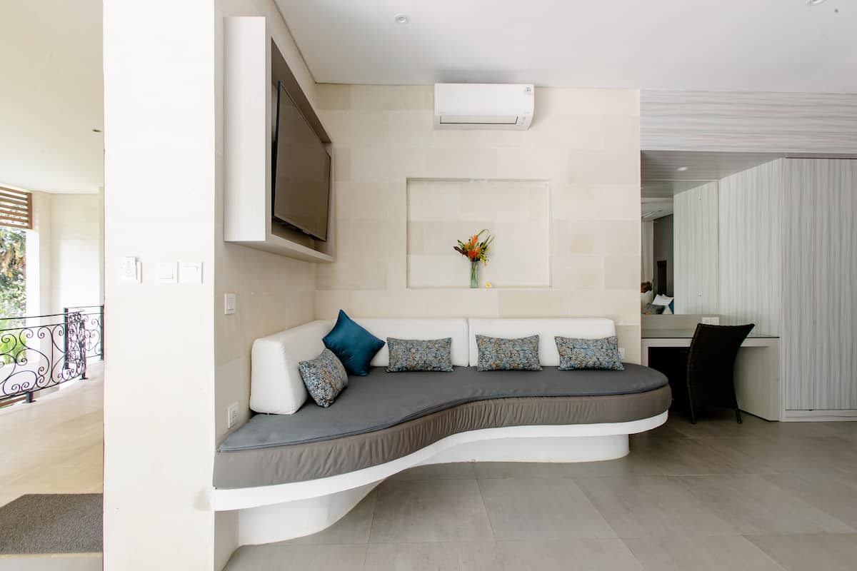 Inviting curved sofa with plush cushions in a bright Balinese space. TV for entertainment, desk for work. Relax in comfort.