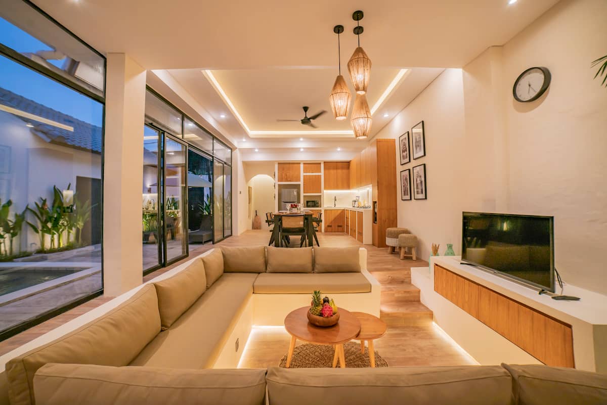 Open living room w/ plush seating, warm lighting & glass doors connecting indoor-outdoor living